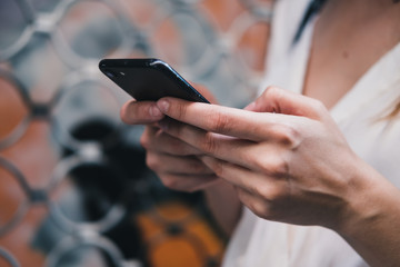 Closeup of girl's hands holding smartphone and typing message. Woman using mobile device to communicate with friends. Modern world communication concept. Orange background.