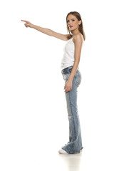 Young pretty woman posing in bell bottom jeans on white background, and pointing on empty space