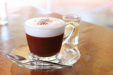 A cup of hot chocolate with foam on top and a shot of sweetened condensed milk on wooden table in the cafe