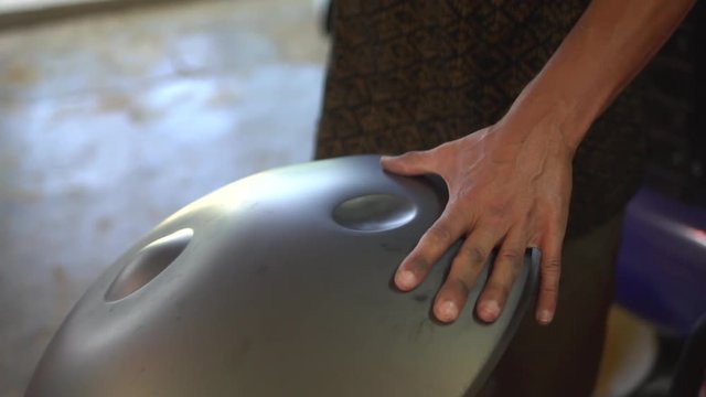 Artisan hands hitting with hammer constructing handpan, a metal percussion instrument. Slow motion.