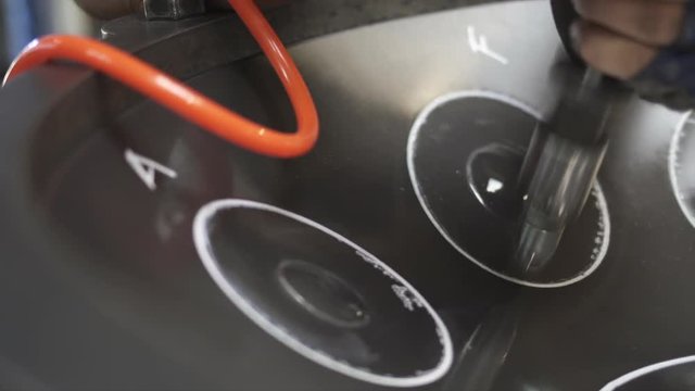 Artisan in his workshop using air hammer to construct a handpan, metal percussion instrument.