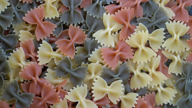 Multicolored pasta background, rotating, top view. Rotation of colored farfalle pasta. Heap of uncooked pasta. Italian food close up. Delicious italian farfalle tricolor pasta, food background