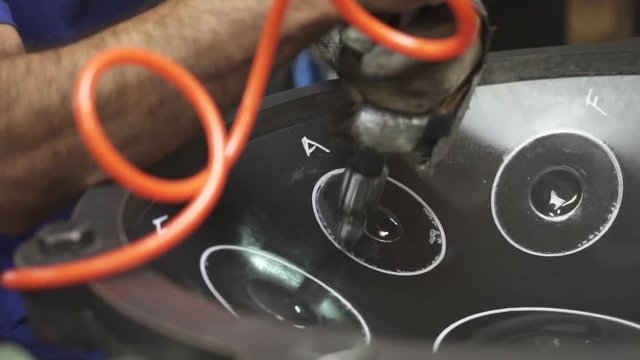 Artisan in his workshop using air hammer to construct a handpan, metal percussion instrument.