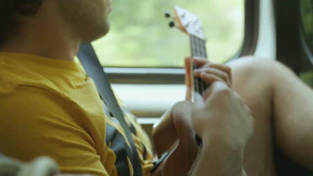 Young male tourist playing ukulele in car