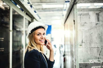 A portrait of an industrial woman engineer on the phone, standing in a factory.