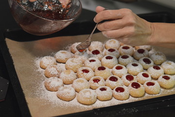 Woman filling warm liquid jam into Christmas cookies that have a hole and are called Engelsaugen or Husarenkrapfen
