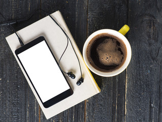 Coffee mug, headphones and book on wooden dark background. Audiobook concept