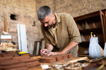 Man in flanel shirt works in his workshop. A joiner is concentrated on his work.