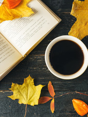 Naklejka na ściany i meble Coffee mug, book and autumn leaves on a dark wooden table