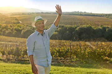 Farmer smiling and waving hand in front of sunset at grape yards
