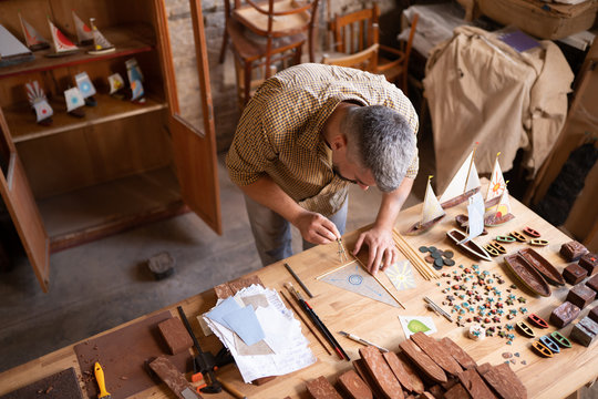 Concentrated carpenter at his working table. A man in his workshop works on drawing a sail of a ship