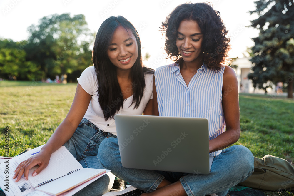 Poster Smiling young friends girls outdoors in park using laptop.