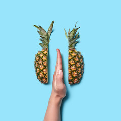 Female hand part with finger half of pineapple on blue background with space for text. Flat lay