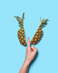 Half of pineapple and female hand. Woman's finger cuts fruit on blue background with space for text. Flat lay