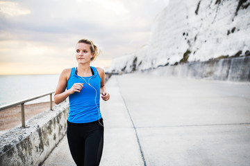 Young sporty woman runner with earphones running on the beach outside.