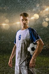 Soccer player on professional soccer night rain stadium. Dirty player in rain drops with football...
