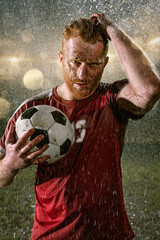 Soccer player on professional soccer night rain stadium. Dirty player in rain drops with football...