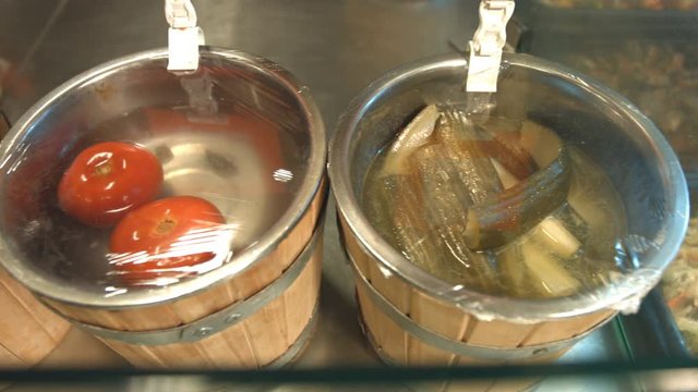 Pickled tomatoes and cucumbers are in kegs.
Pickled tomatoes and cucumbers in kegs lined up in a line. Сamera moves from left to right along the shelf.