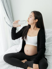 Asian pregnant woman drinking a bottle of water after finished exercise, lifestyle concept.