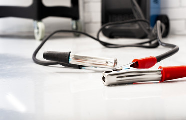 red and black clamps for charging battery car with electricity lying on the floor in car repair garage