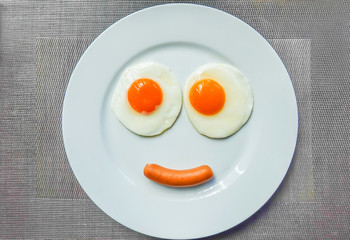 Top view of fried egg and sausage smiley face on white plate , breakfast serve for kid