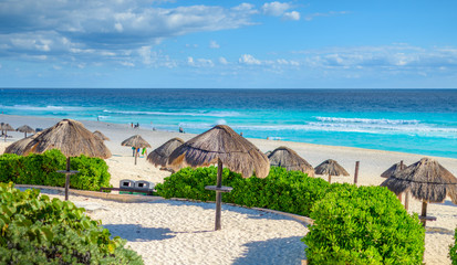 Cancun beach in mexico with umbrellas in the sand, beautiful blue water with dramatic clouds