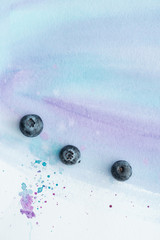 top view of fresh blueberries on white surface with purple watercolor strokes and blots