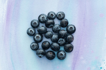top view of heap of blueberries on white surface with purple watercolor strokes