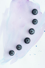 top view of row of blueberries on white surface with purple watercolor strokes