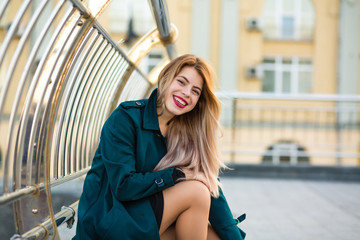 Happy blonde model wearing green coat posing at the street. Space for text