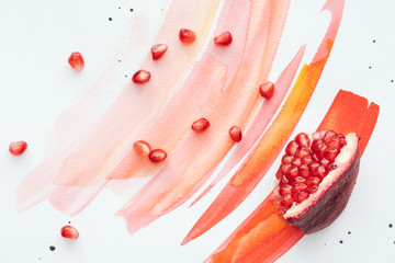 top view of pomegranate piece with seeds on white surface with red watercolor strokes