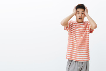 Portrait of shocked young asian guy in stupor pressing hands to head open mouth from amazement,...