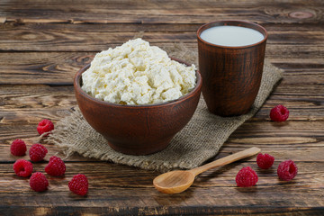 Cottage cheese and milk in clayware on wooden table, sackcloth table-napkin and wooden spoon