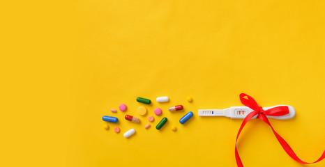 Pregnancy test, pills and vitamins on a yellow background.