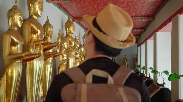 Young Asian traveling backpack tourist walking inside in Wat Pho Temple with golden buddha statues in the row in Bangkok, Thailand - Travel Backpack Explore in Asia City Concept