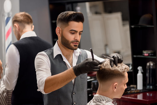 Serious barber making stylish haircut using comb and razor.