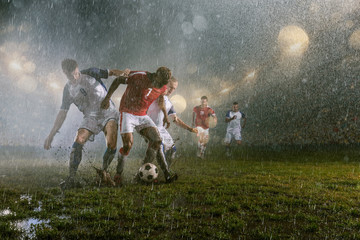 Obraz na płótnie Canvas Soccer players performs an action play on a professional night rain stadium. Dirty players in rain drops scores a goal. Grass in the stadium wet from the rain