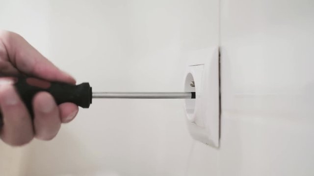 Close up shot of tmans hand fixing servicing electricity socket at home, home improvements with popular tools