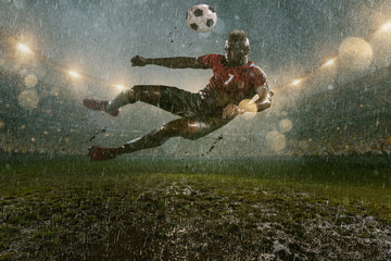 Fototapeta na wymiar Soccer player on professional soccer night rain stadium. Dirty player in rain drops kicks the football ball in flight