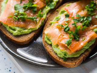 Rye bread avocado toasts with smoked salmon on white wooden board