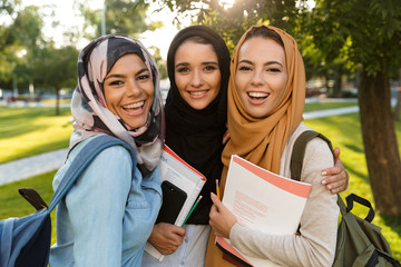 Arabian women students holding books in park outdoors.