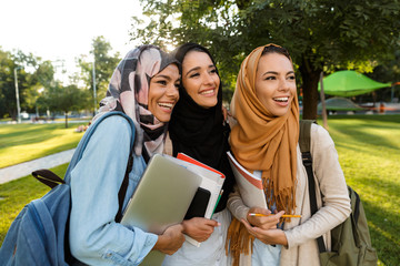 Arabian women students holding books in park outdoors.