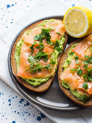 Rye bread avocado toasts with smoked salmon on white wooden board
