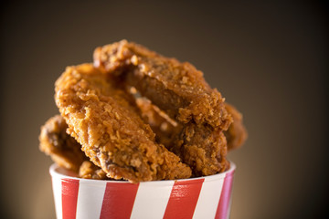 Bucket full of crispy kentucky fried chicken with smoke on brown background. Selective focus.