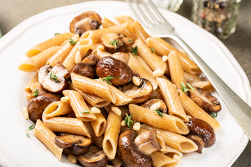 Homemade whole grain pasta penne with fried mushrooms and thyme on white plate. Delicious healthy italian vegetarian food background.