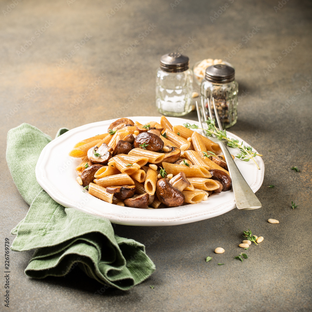 Wall mural Homemade whole grain pasta penne with fried mushrooms and thyme on white plate. Delicious healthy italian vegetarian food background. Copy space.