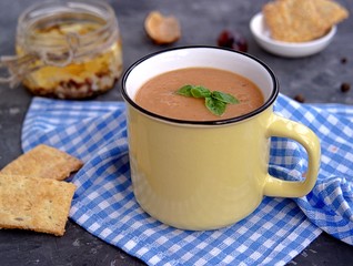 Soup puree from baked aubergines and tomatoes in a yellow mug. Served with feta cheese and crackers.