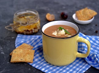 Soup puree from baked aubergines and tomatoes in a yellow mug. Served with feta cheese and crackers.