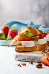 Fresh sandwich with croissant with goat cheese, strawberries, honey and pecans on wooden cutting board with copy space.