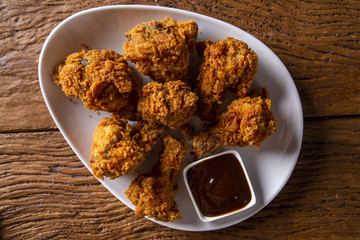Bucket full of crispy kentucky fried chicken with smoke and barbecue sauce on brown background. Selective focus.